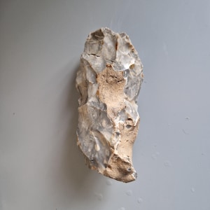May include: A gray and brown flint hand axe with a rough, chipped surface.