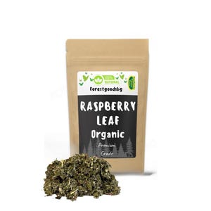 May include: A brown paper bag with a label that reads "Raspberry Leaf Organic Premium Grade" and a green logo that says "100% Natural forestgoodsbg". A pile of dried raspberry leaves is in front of the bag.