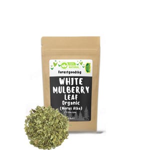 Könnte beinhalten: Ein brauner Papiersack mit einem weißen Etikett mit dem Text "WHITE MULBERRY LEAF Organic (Morus Alba) Premium Grade". Ein Haufen getrockneter grüner Blätter liegt vor dem Beutel.