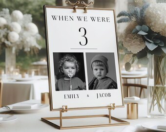 May include: A white table number card with black text that reads "When we were 3" and features two black and white photos of children. The text below the photos reads "Emily & Jacob". The card is on a gold metal stand.
