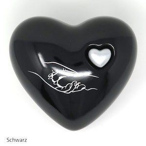 May include: A black heart-shaped decorative object with a small, silver heart inset. A white line drawing of two hands clasped is on the front. The word "Schwarz" is at the bottom.