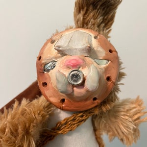 Könnte beinhalten: Ein braunes und weißes Plüschtier mit einem modelliertem Gesicht. Das Gesicht hat eine runde, braune, strukturierte Basis mit einer weißen Nase, einem rosa Mund und zwei weißen Stoßzähnen. Das Spielzeug hat ein braunes Seil um den Hals.
