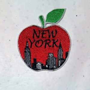 Peut inclure: Écusson brodé en forme de pomme rouge avec une feuille verte. Le patch présente le texte "NEW YORK" en noir, avec une ligne d'horizon noire et blanche de New York.