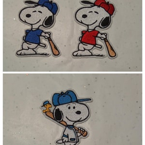 Op de afbeelding: Geborduurde patches met Snoopy in honkbaloutfits. Twee patches tonen Snoopy in blauwe en rode honkbaluniformen, met een knuppel. De derde patch toont Snoopy in een honkbaluniform met een honkbalknuppel en Woodstock.