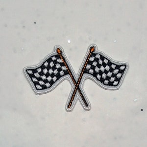 May include: Embroidered patch featuring two crossed checkered racing flags. The flags are black and white, with a gray border and orange-tipped poles. The patch is designed for application on clothing or accessories.