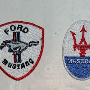 Puede incluir: Dos parches bordados: un escudo Ford Mustang con un caballo corriendo y el texto "FORD MUSTANG", y un óvalo Maserati con un tridente rojo y el texto "MASERATI".