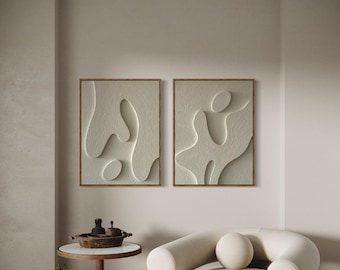 May include: Two framed abstract art prints with a white textured design on a beige wall. A white armchair with a round back and a small round table with a wooden top and a black metal base are in the foreground.