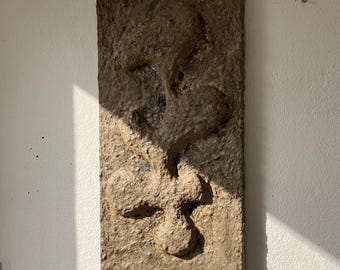 May include: A rectangular, textured, brown wall sculpture with an abstract design. The sculpture has raised, organic shapes and is mounted on a white wall. The artwork is illuminated by natural light, creating shadows and highlighting the texture.