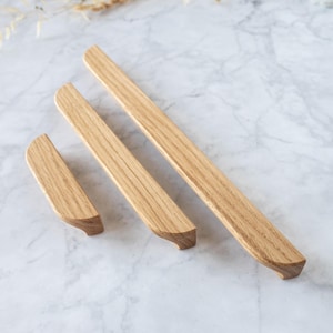 Op de afbeelding: Drie houten kastgrepen in verschillende maten. De grepen zijn gemaakt van lichtbruin hout met een natuurlijke houtnerf.