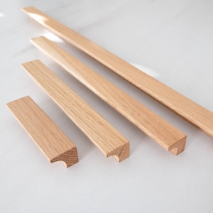 Può includere: Quattro maniglie per armadi in legno di diverse dimensioni. Le maniglie sono in legno marrone chiaro e hanno un design semplice e arrotondato.