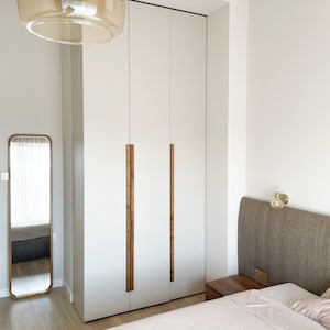 May include: White closet doors with wooden handles in a bedroom with a bed and a mirror. The closet doors are closed.