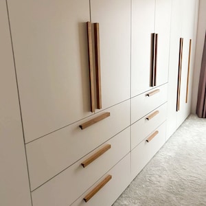 Op de afbeelding: Witte kastdeuren met meerdere laden en houten handgrepen. De kastdeuren zijn gesloten en de laden zijn open.