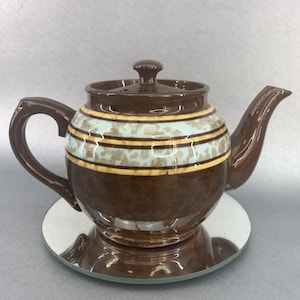 May include: A brown teapot with a light blue and yellow striped design. The teapot has a round body and a lid with a knob on top. It is sitting on a silver-colored circular stand.