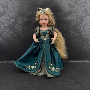 May include: A porcelain doll with long blonde hair and a teal satin gown. The dress features gold embroidery with white floral accents. The doll wears a gold and pearl crown. The doll's dress is open in the front, revealing a gold and brown underdress.