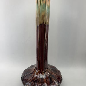 Op de afbeelding: Een decoratieve vaas met een uitlopende basis en een slanke hals. De vaas heeft een glanzende bruine afwerking aan de onderkant, die overgaat in groen en goud aan de bovenkant. De basis heeft een gestructureerd, bladachtig ontwerp.