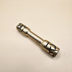 May include: A metallic, cylindrical tool with a central shaft and flared ends. The ends feature a series of etched, dark lines. The tool has a brushed metal finish and is set against a neutral background.