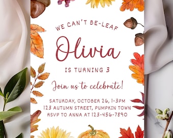 May include: A rectangular birthday invitation card with a white background featuring watercolor illustrations of sunflowers, orange and red autumn leaves, acorns, and a pumpkin. The text reads: WE CAN'T BE-LEAF Olivia IS TURNING 3 Join us to celebrate!