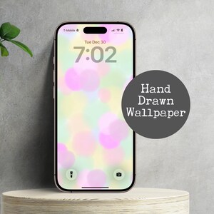 May include: A smartphone displays a hand-drawn wallpaper with soft, colorful bokeh effects in pink, yellow, and green. The screen shows the time and date. A dark gray circle with the text "Hand Drawn Wallpaper" is on the right.