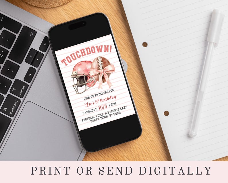 May include: A smartphone displays a pink football-themed birthday invitation. The invitation features a pink football helmet and football with a bow, and the text "TOUCHDOWN!" The phone rests on a wooden surface next to a laptop and a notepad.
