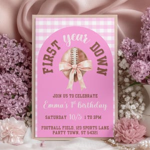 Puede incluir: Invitación rosa y beige para una fiesta de primer cumpleaños. El diseño presenta un balón de fútbol con un lazo, las palabras "First Down" y "year" en arco, y detalles de la fiesta. Rodeado de flores rosas.