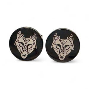 May include: A pair of black round stud earrings. Each earring features a silver wolf head design with Celtic knot details. The earrings are set against a white background.