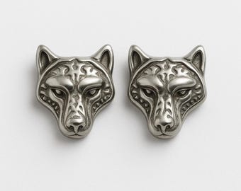 May include: Two silver-colored wolf head studs. Each stud features detailed facial features, including eyes, nose, and decorative patterns. The studs are symmetrical and have a slightly aged appearance, suggesting a vintage or antique style.