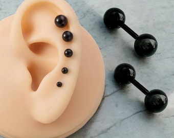 May include: A close-up of a black barbell earring with two black balls on each end. The earring is shown on a model ear with multiple black pearl studs.