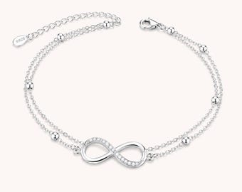 May include: A double-strand silver bracelet featuring a central infinity symbol charm encrusted with small clear stones. The chain includes evenly spaced small silver beads and an adjustable extension chain with a tag stamped with 925.