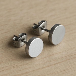 Op de afbeelding: Een paar zilveren oorbel studs met een cirkelvormig ontwerp. De oorbellen hebben een geborstelde afwerking.