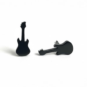 May include: A pair of black guitar-shaped stud earrings. The earrings are small, with a simple, solid design. One earring is upright, and the other is lying on its side. The background is plain white.