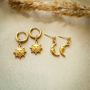 Könnte beinhalten: Ein Paar goldene Creolen mit einem Sonnenanhänger und ein Paar goldene Ohrstecker mit einem Halbmondanhänger.