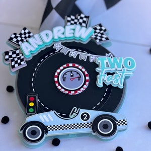 Puede incluir: Un coche de carreras azul y blanco con un diseño de bandera a cuadros. El coche está en una pista de carreras negra con una línea de meta de bandera a cuadros. Las palabras "Andrew Two Fast" están en la pista.