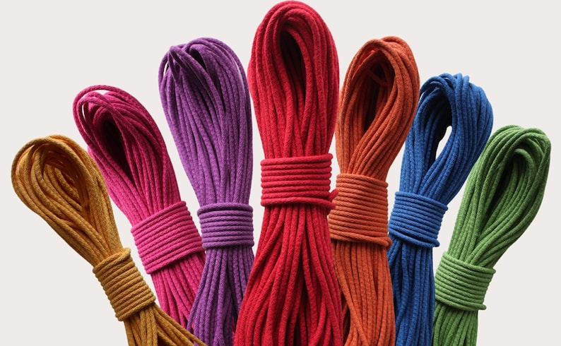 May include: A collection of seven bundles of braided cord arranged in a fan shape. The cords are colored in mustard yellow, magenta, purple, red, burnt orange, royal blue, and lime green. Each bundle is neatly coiled and secured with a central wrap.