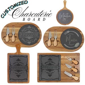 Op de afbeelding: Aangepaste charcuterieplanken in verschillende vormen, gemaakt van hout en leisteen. De planken zijn ovaal, rond en rechthoekig. Elke plank heeft een leisteen inzetstuk met gepersonaliseerde tekst, zoals "Martin Family" en een citaat. Kaasmes en vorken zijn inbegrepen.