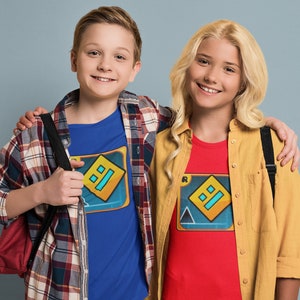 May include: Two kids wearing blue and red t-shirts with a yellow and blue graphic design. The graphic design features a square with a blue and yellow pattern inside. The kids are wearing plaid shirts over their t-shirts. The girl is wearing a yellow plaid shirt and the boy is wearing a red and black plaid shirt.