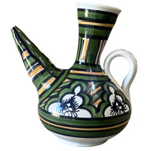 May include: A ceramic pitcher with a long spout and a handle. The pitcher is painted with a green, white, and gold floral design. The base and handle are white, and the spout is angled.