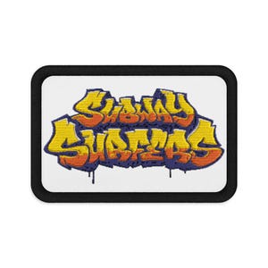 Puede incluir: Un parche rectangular bordado con fondo blanco y un borde negro grueso. En el centro, el texto Subway Surfers aparece en una fuente de grafiti estilizada, coloreada en amarillo y naranja con un contorno morado oscuro y detalles de goteo.