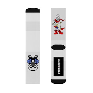 May include: A pair of white socks with a pixelated image of a skeleton character from the video game Undertale. One sock features the character Papyrus, while the other sock features the character Sans. The socks have black trim and the text "UNDERTALE" is printed on one sock.