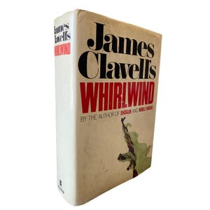 Op de afbeelding: Een hardcover boek met de titel "James Clavell's Whirlwind". De kaft is gebroken wit met zwarte en rode tekst. De naam van de auteur staat in grote zwarte letters en de titel in rood. Een groene figuur is afgebeeld.