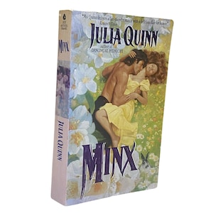 Pode incluir: Um livro de bolso intitulado "Minx" de Julia Quinn. A capa apresenta um casal abraçado em um campo de flores brancas. O nome do autor e uma citação da Romantic Times são visíveis.