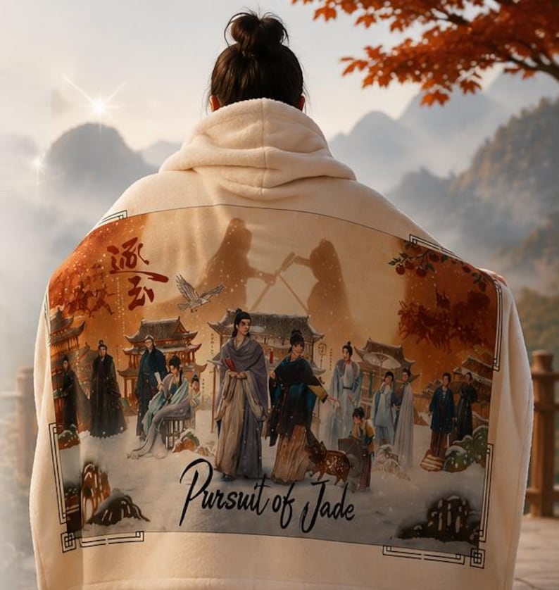 Op de afbeelding: Cr&egrave;mekleurige hoodie met een gedetailleerde illustratie op de rug. Het kunstwerk toont een sc&egrave;ne met figuren in traditionele kledij, gebouwen en de tekst "Pursuit of Jade". Het ontwerp heeft een vintage esthetiek.