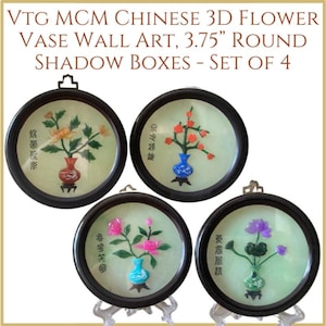 May include: Set of four 3.75 inch round shadow boxes featuring Chinese flower vase wall art. Each box has a different flower design with jade-like flowers and leaves in a vase. The boxes have black frames and are displayed on small stands.