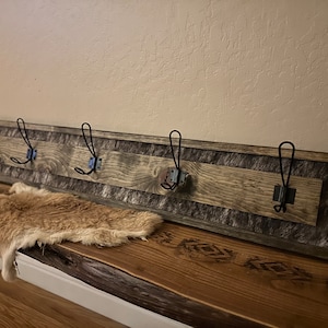 May include: A rustic wooden coat rack with four black metal hooks. The rack features a distressed wood finish with a faux fur panel. The rack is mounted on a wooden bench with a decorative pattern.