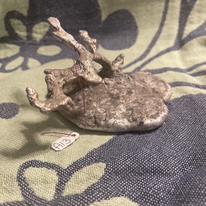 May include: A silver-colored, abstract, organic-shaped sculpture with a rough, textured surface. The sculpture is tagged with a white label that says "A13".