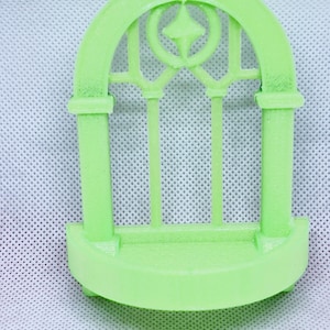 May include: A light green plastic archway with a decorative design. The archway has a small shelf at the bottom.