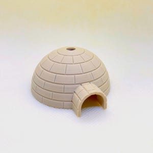 May include: A small, beige, plastic igloo with a rounded top and a rectangular entrance. The igloo is made to look like it is made of bricks.