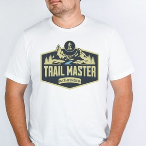 May include: White t-shirt with a graphic of a mountain range and a river, with the text "TRAIL MASTER PATHFINDER" in a gold and black logo.