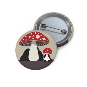 Pode incluir: Um botão com uma ilustração de desenho animado de dois cogumelos vermelhos e brancos com hastes brancas. O cogumelo maior está no fundo e o menor em primeiro plano. Os cogumelos estão sobre um fundo castanho.