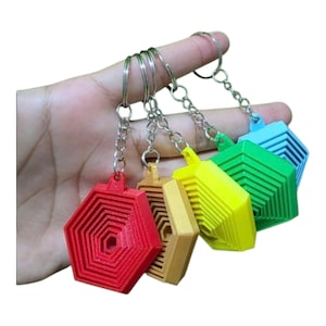 May include: A set of five hexagonal keychains in red, gold, yellow, green, and blue. Each keychain features a concentric, tiered geometric design with a central hole, attached to a silver-toned metal split ring by a short chain link connector.