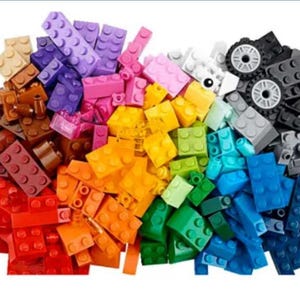 Pode incluir: Uma vibrante variedade de blocos de construção coloridos em várias formas e tamanhos. Os blocos são em tons de vermelho, laranja, amarelo, verde, azul, roxo e castanho. Alguns blocos pretos com rodas também estão presentes, sugerindo um brinquedo de construção.